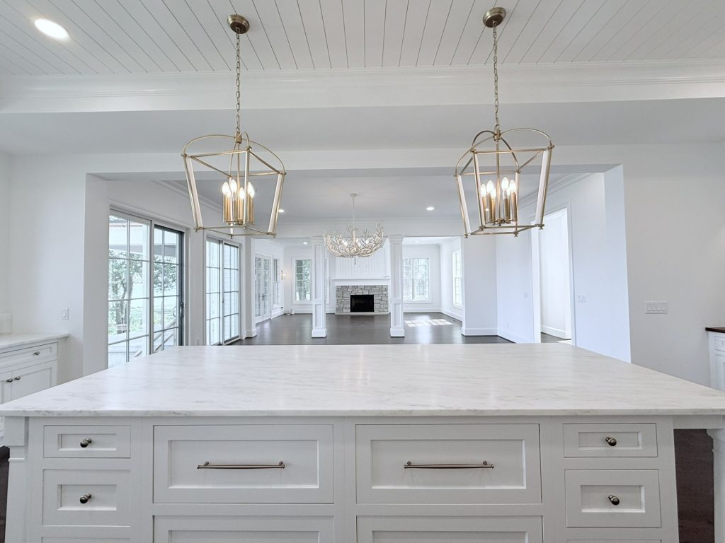 Kitchen island area with brass cage pendant lights, opening into a great room with a stone fireplace and staircase