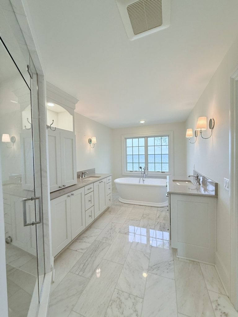 Primary bathroom with his-and-her vanities, a glass shower enclosure, freestanding tub, and lake-view window