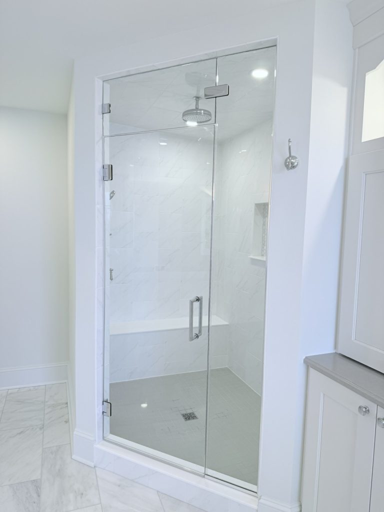 Frameless glass shower enclosure with a rainfall shower head, tile bench seat, and mosaic niche