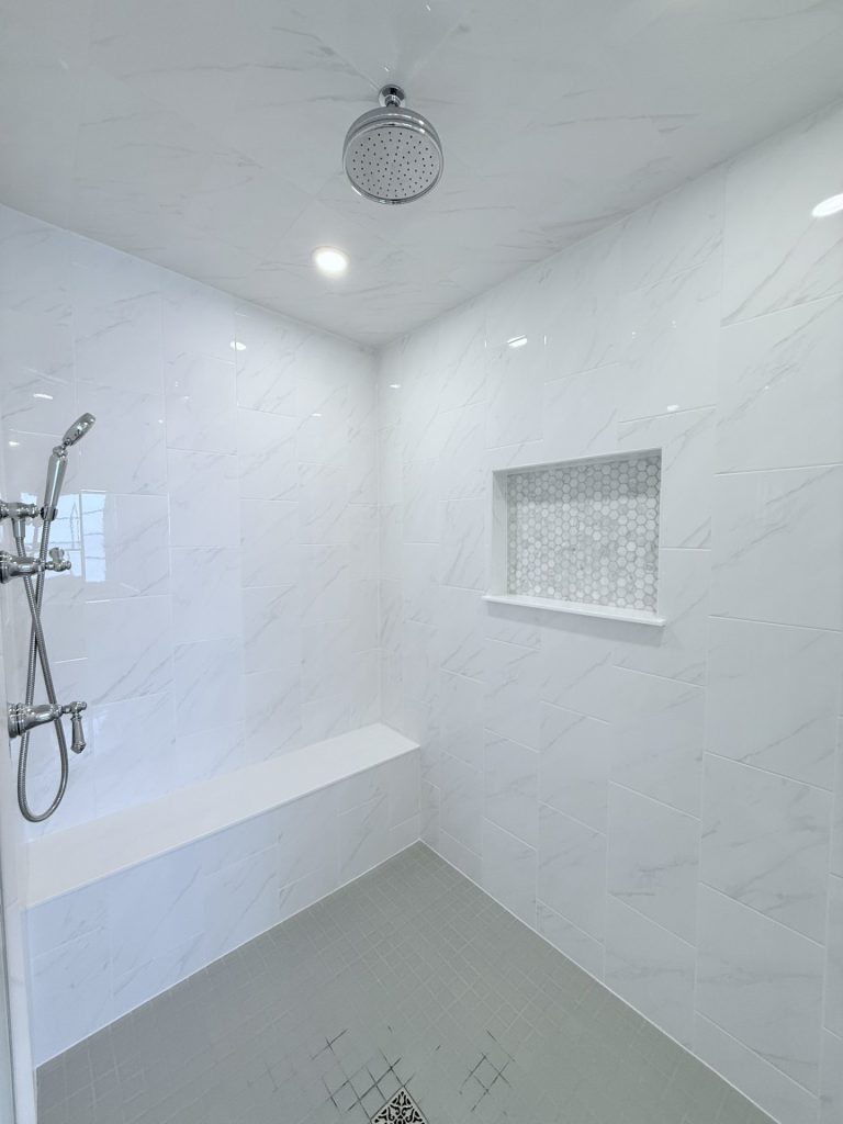 Walk-in tiled shower with a rainfall shower head, mosaic tile niche, and teak-look bench seat