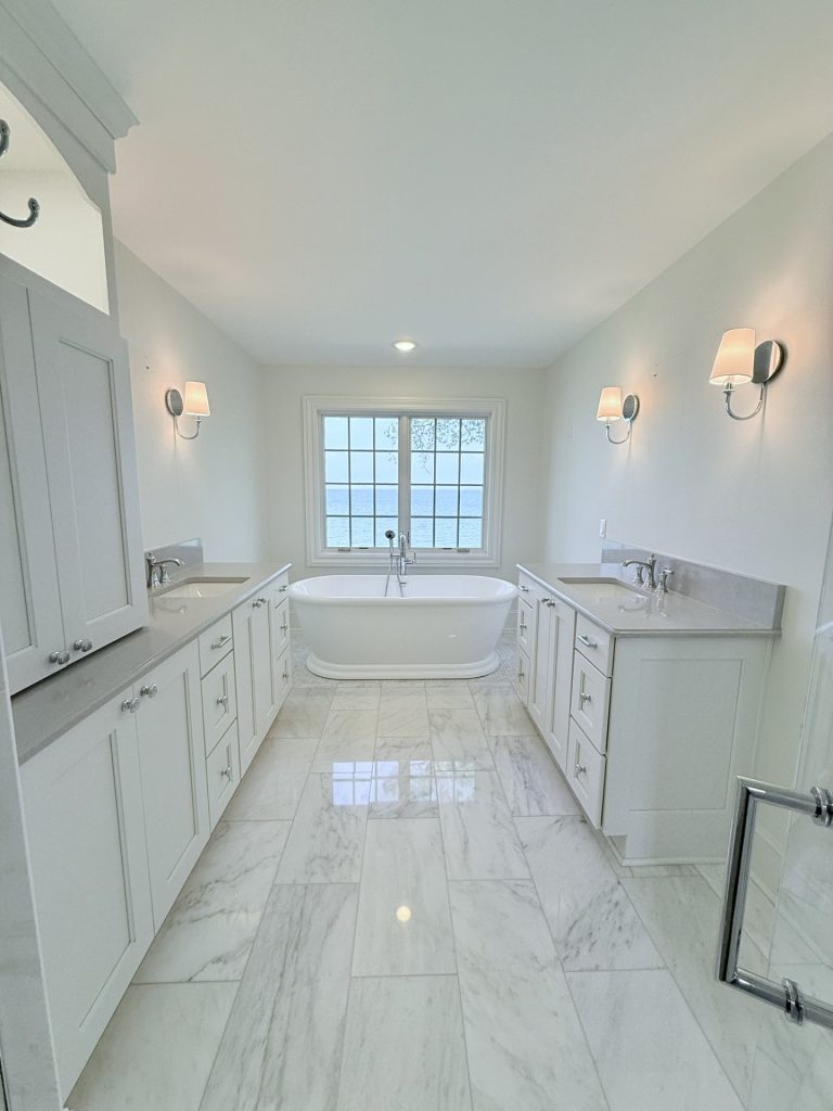 Primary bathroom with double vanities flanking a freestanding soaking tub and a window with a lake view