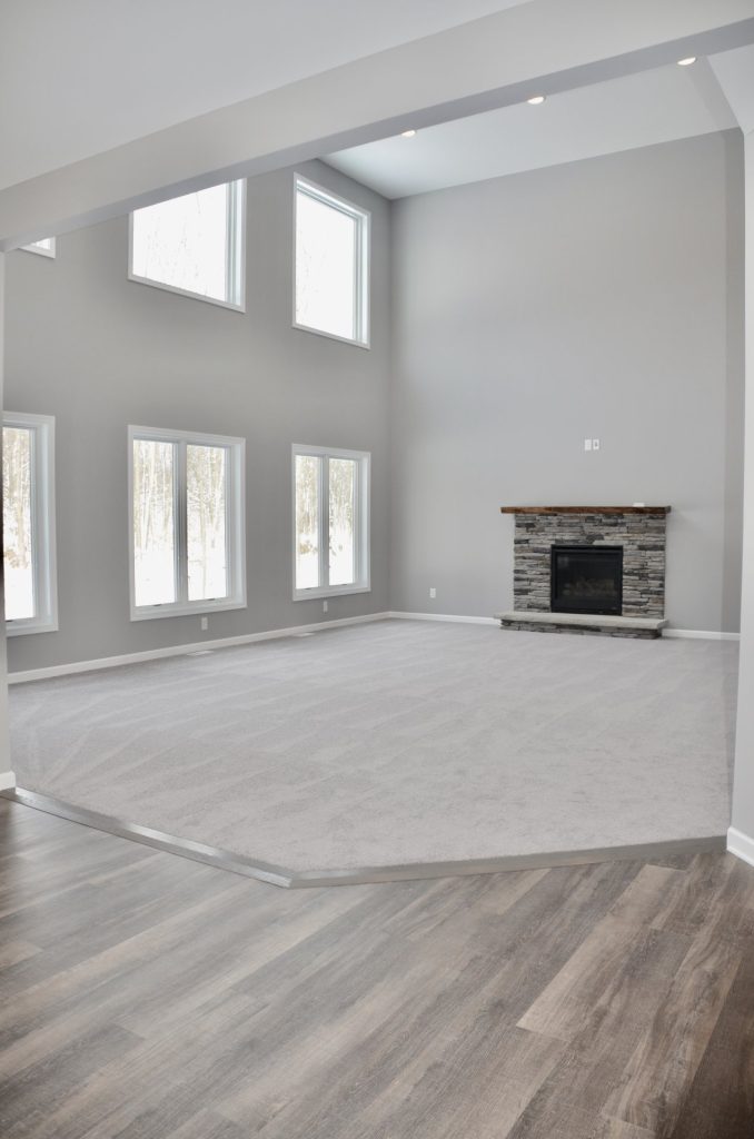Bradford-Two-Story-Great-Room-with-Stone-Fireplace-Tall-Windows-and-Light-Carpet