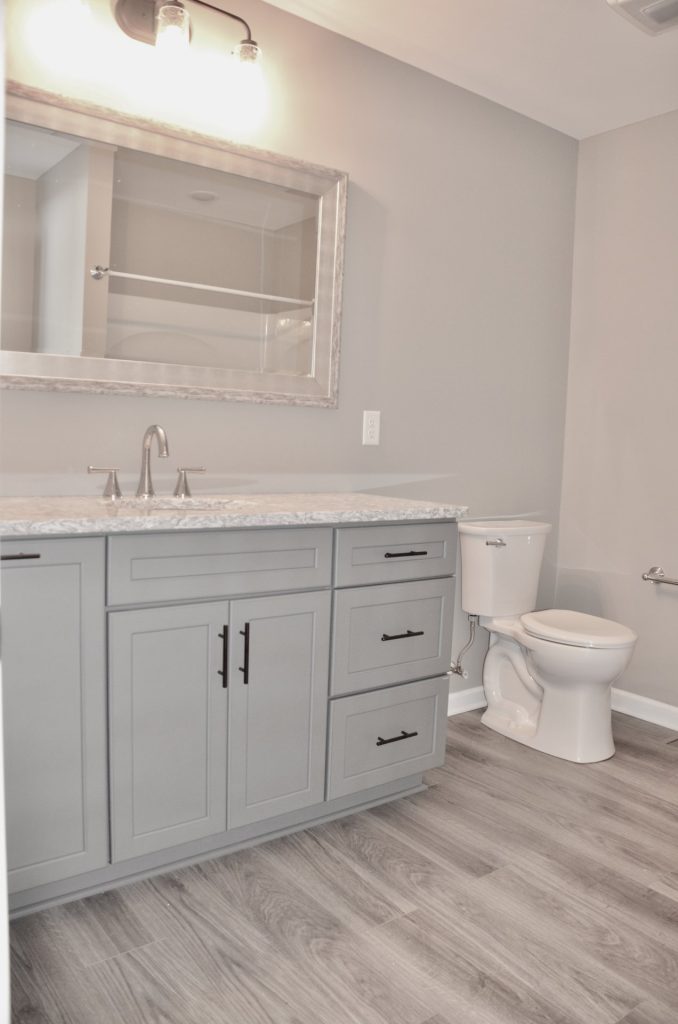 Bradford-Full-Bathroom-with-Gray-Vanity-Large-Mirror-Toilet-and-Wood-Look-Flooring