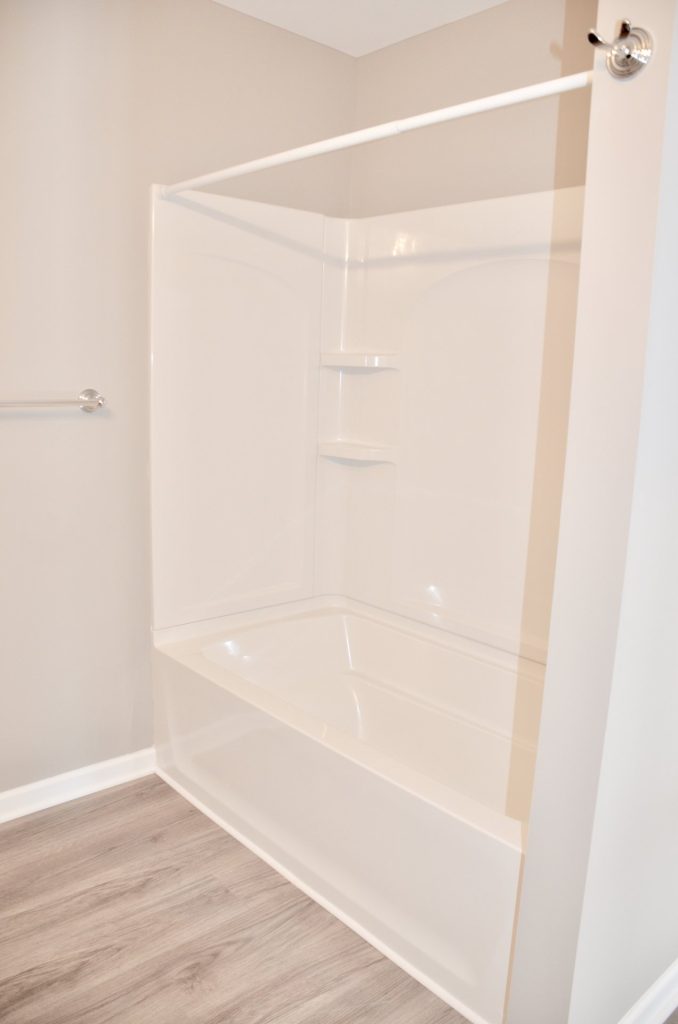 Bradford-Tub-Shower-Combo-with-White-Surround-Built-In-Shelves-and-Wood-Look-Flooring