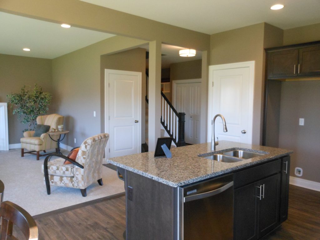 The Concord II Kitchen with Dark Cabinetry, Granite Island, Stainless Sink, Wood-Look Flooring & Open Great Room View