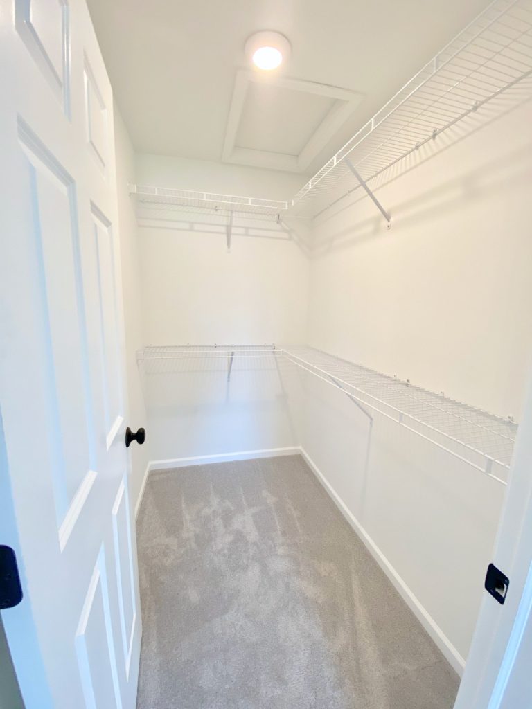 The Forsythe Walk-In Closet with Wraparound Shelving, Attic Access Panel, Light Carpet & White Walls