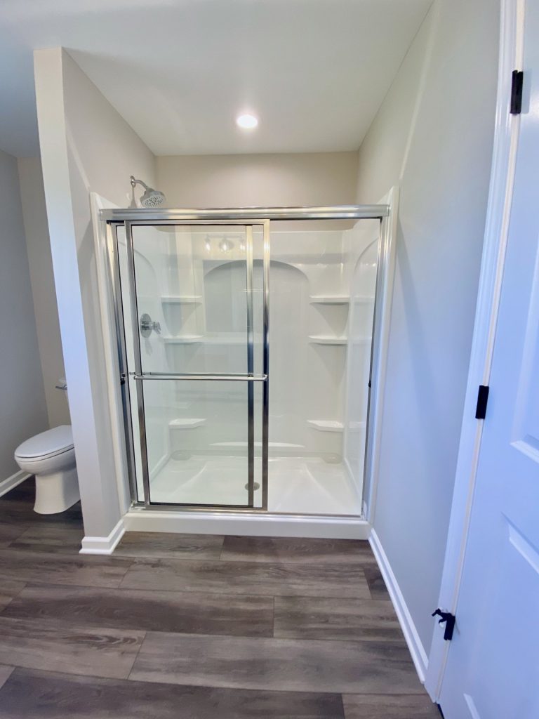 The Forsythe Walk-In Shower with Sliding Glass Doors, White Surround, Built-In Shelves & Tile Flooring