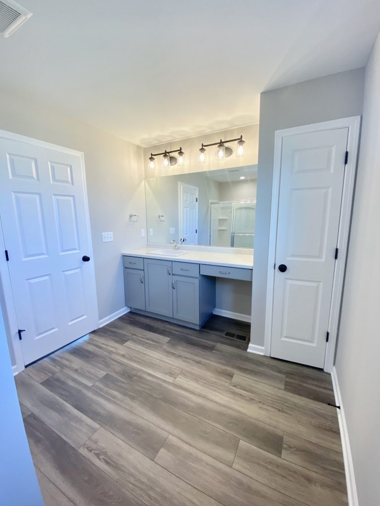The Forsythe Primary Bathroom with Gray Vanity, Large Mirror, Tile Flooring, Makeup Knee Space & White Doors