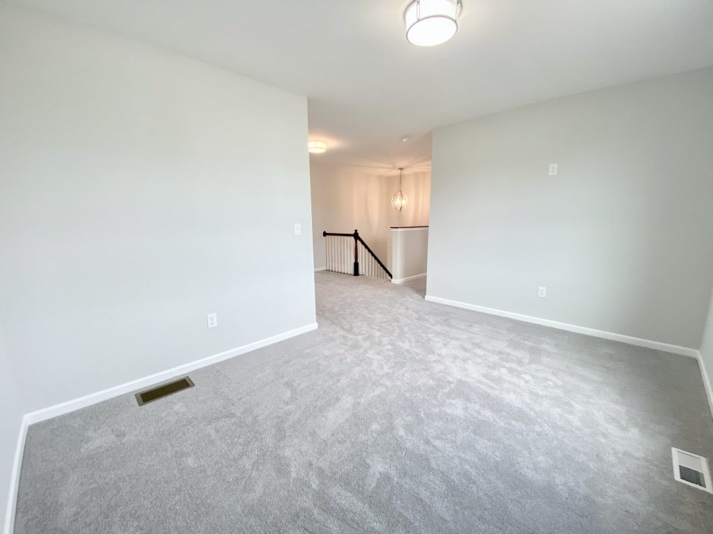 The Forsythe Bedroom with Light Carpet, Open Loft View, Neutral Walls & Flush-Mount Ceiling Light