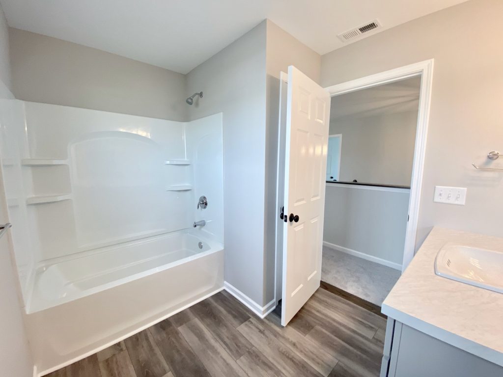 The Forsythe Tub-Shower Combo with White Surround, Built-In Shelves, Tile Flooring & Hallway View