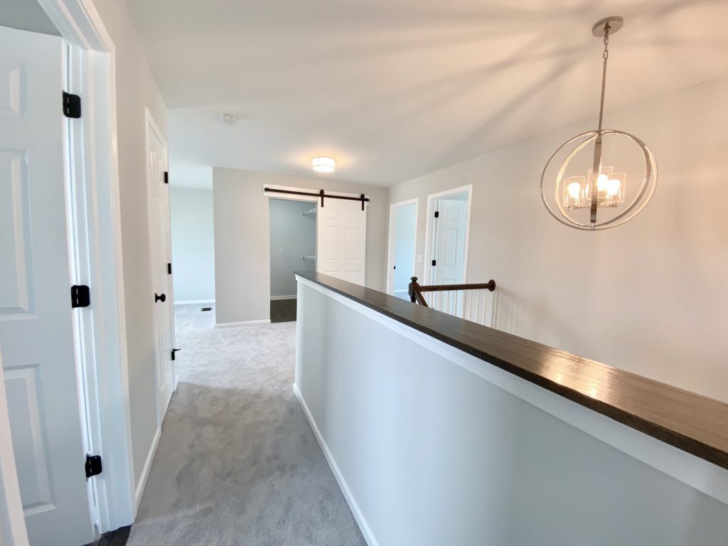 The Forsythe Upper Hallway with Dark Cap Rail, Pendant Chandelier, Barn Door & Light Carpet