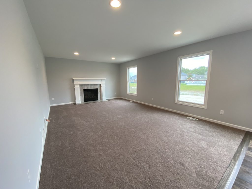 The Mackenzie Great Room with Fireplace, Neutral Carpet, Two Tall Windows & Gray Walls
