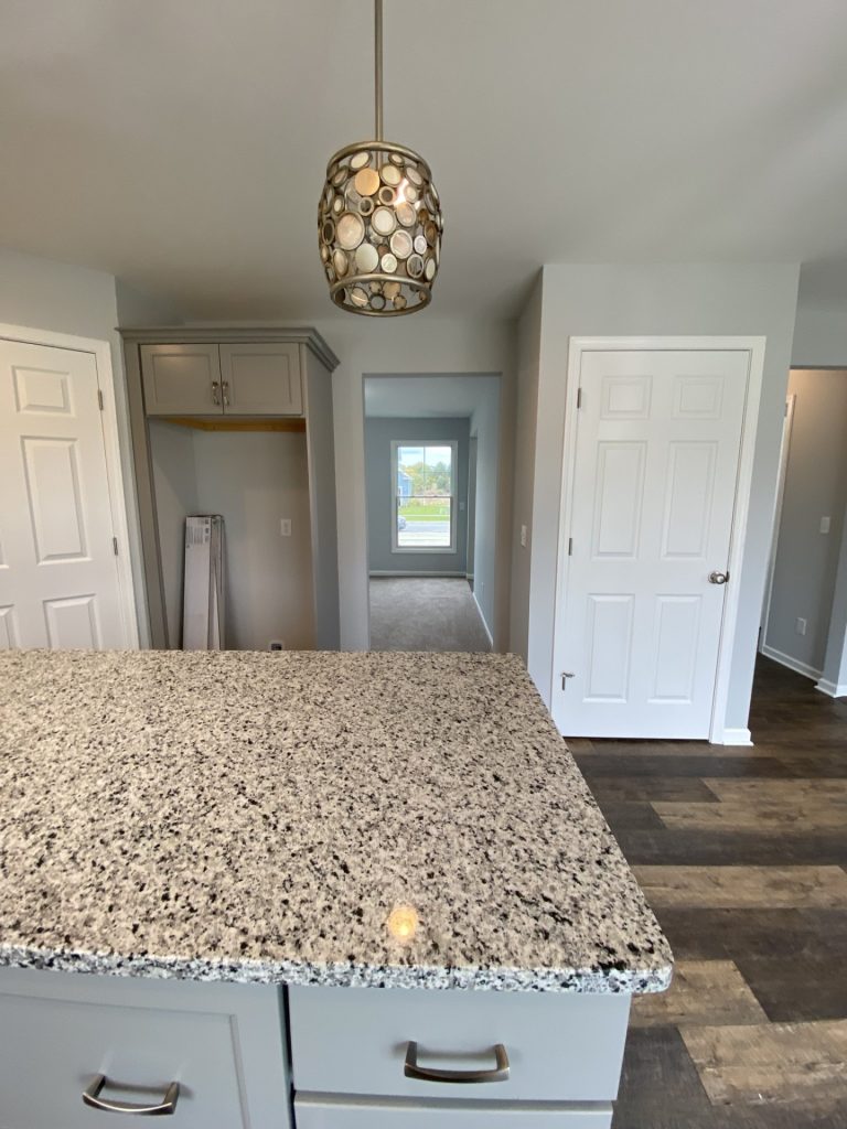The Mackenzie Kitchen Close-Up View of Kitchen Island with Neutral Granite Counter under Pendant Lighting