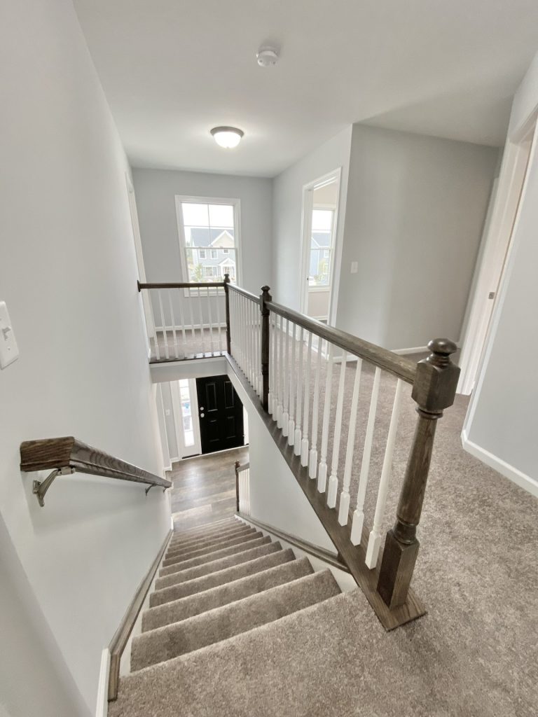 The Mackenzie Upper Hallway with Stair Opening, Neutral Carpet, Front Door View & White Balusters