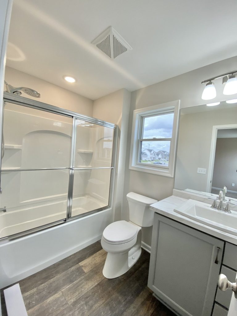 The Mackenzie Full Bathroom with Gray Vanity, Tub-Shower Combo, Window Light & Wood-Look Flooring