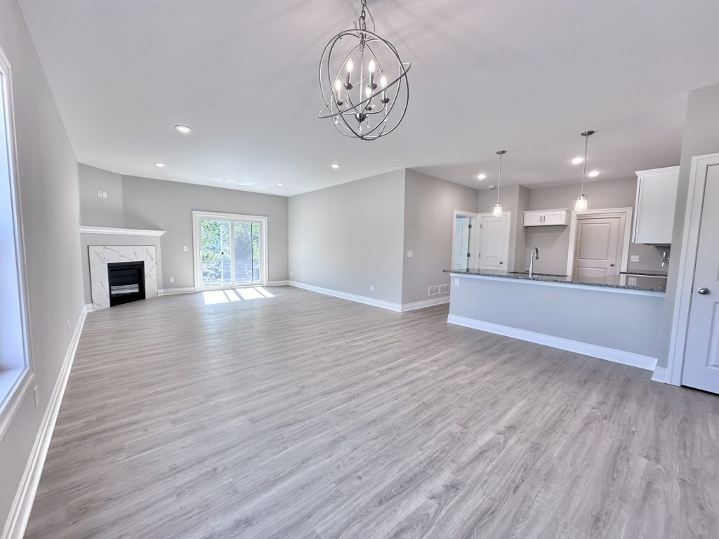 Open-Sunlit-Living-Area-with-Kitchen-in-Background-in-Whites-Neutrals-with-Patio-Entrance-and-Fireplace