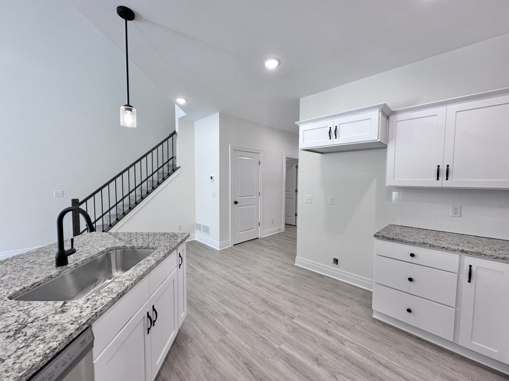 Madison-Kitchen-with-White-Cabinetry-Granite-Counters-Black-Faucet-and-Staircase-View
