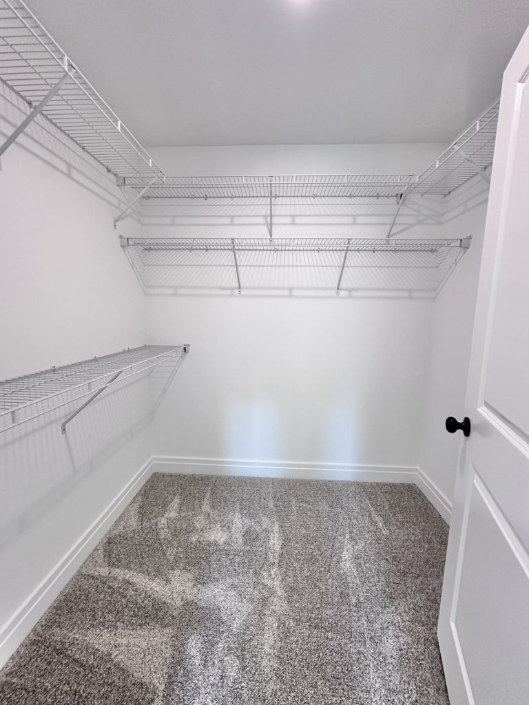 Madison-Secondary-Walk-In-Closet-with-Gray-Carpet-Wraparound-Wire-Shelving-and-White-Walls