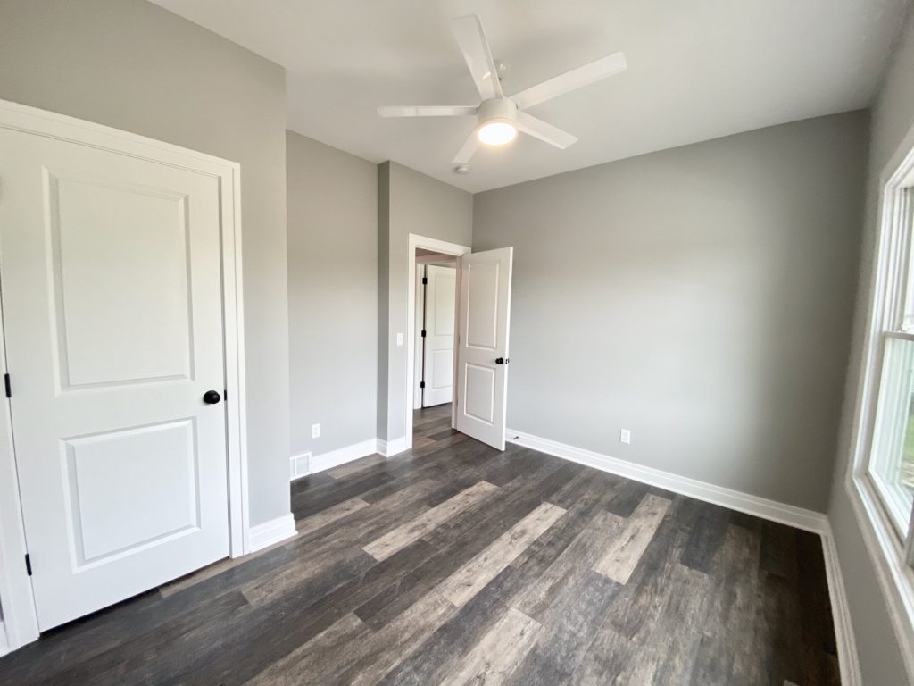 The Golden Bedroom with Walk-In Closet Entry, Gray Walls, White Ceiling Fan & Wood-Look Flooring