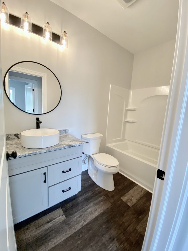 The Golden Full Bathroom with Gray Vanity, Tub-Shower Combo, Round Mirror & Wood-Look Flooring