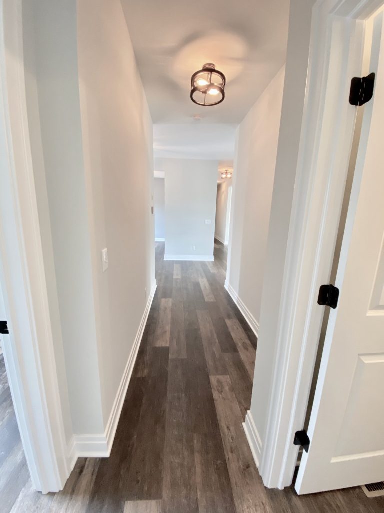 The Golden Hallway with Wood-Look Flooring, White Trim, Neutral Walls & Open Room View