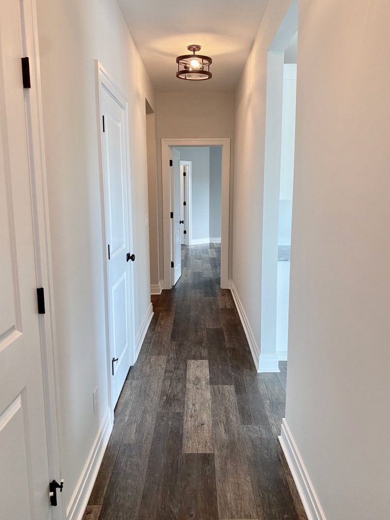 The Golden Hallway with Wood-Look Flooring, White Trim, Neutral Walls & Bathroom Entry