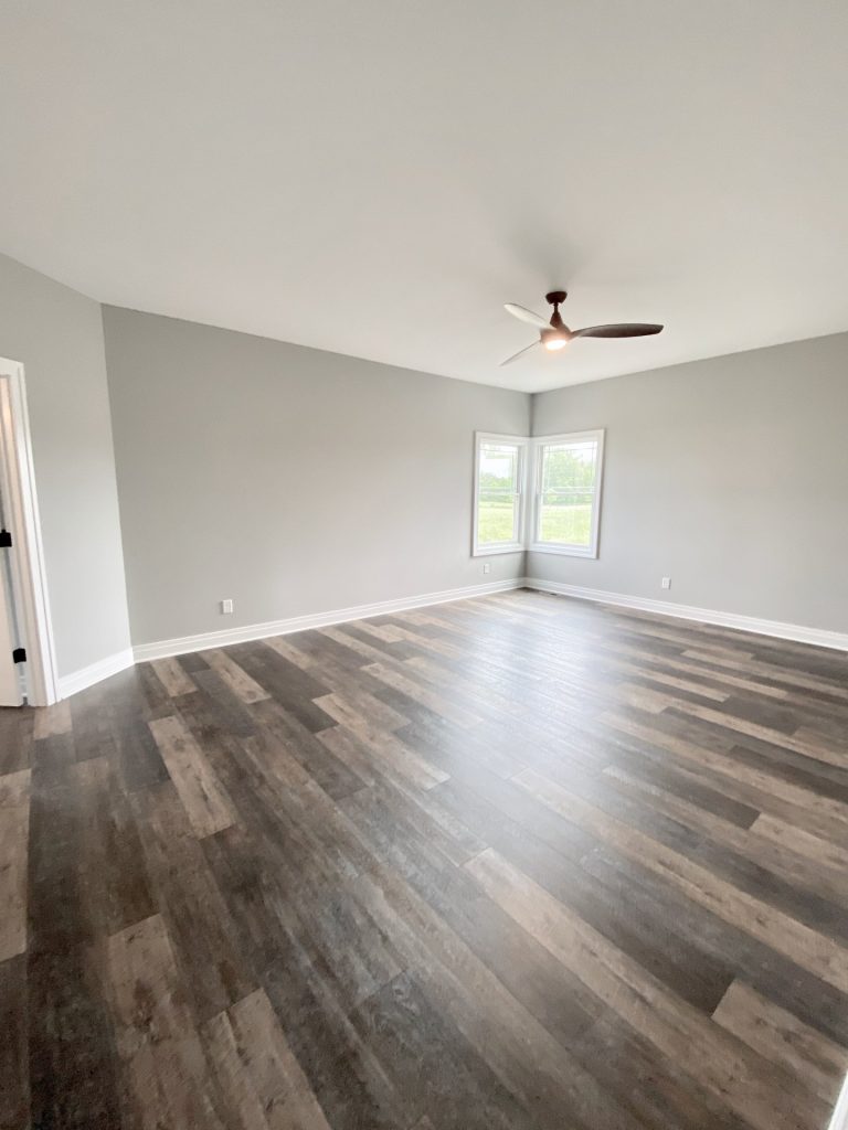 The Golden Primary Bedroom with Corner Windows, Gray Walls, Ceiling Fan & Wood-Look Flooring