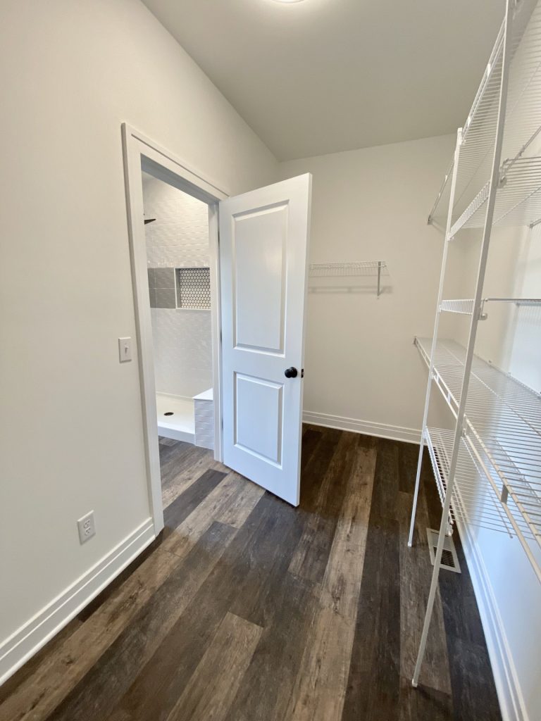 The Golden Walk-In Closet with Bathroom Entry, Wire Shelving, White Walls & Wood-Look Flooring