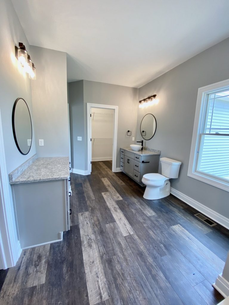 The Golden Primary Bathroom with Dual Vanities, Round Mirrors, Window Light & Wood-Look Flooring