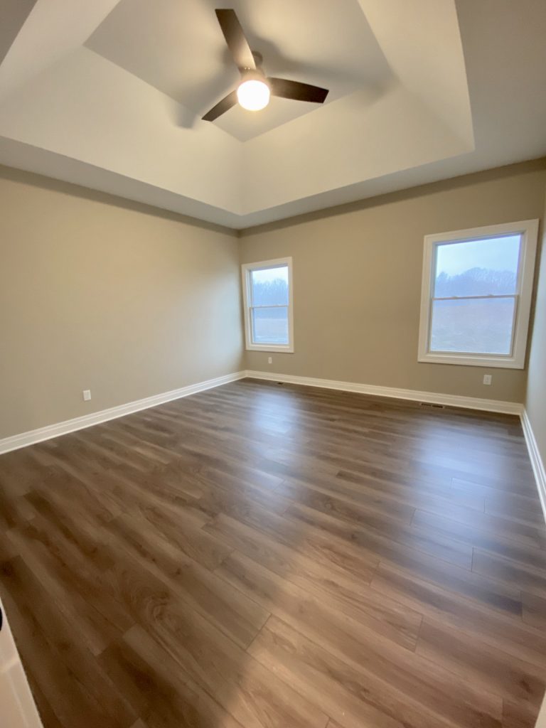 The Portsmouth Primary Bedroom with Tray Ceiling, Ceiling Fan, Two Windows and Wood-Look Flooring