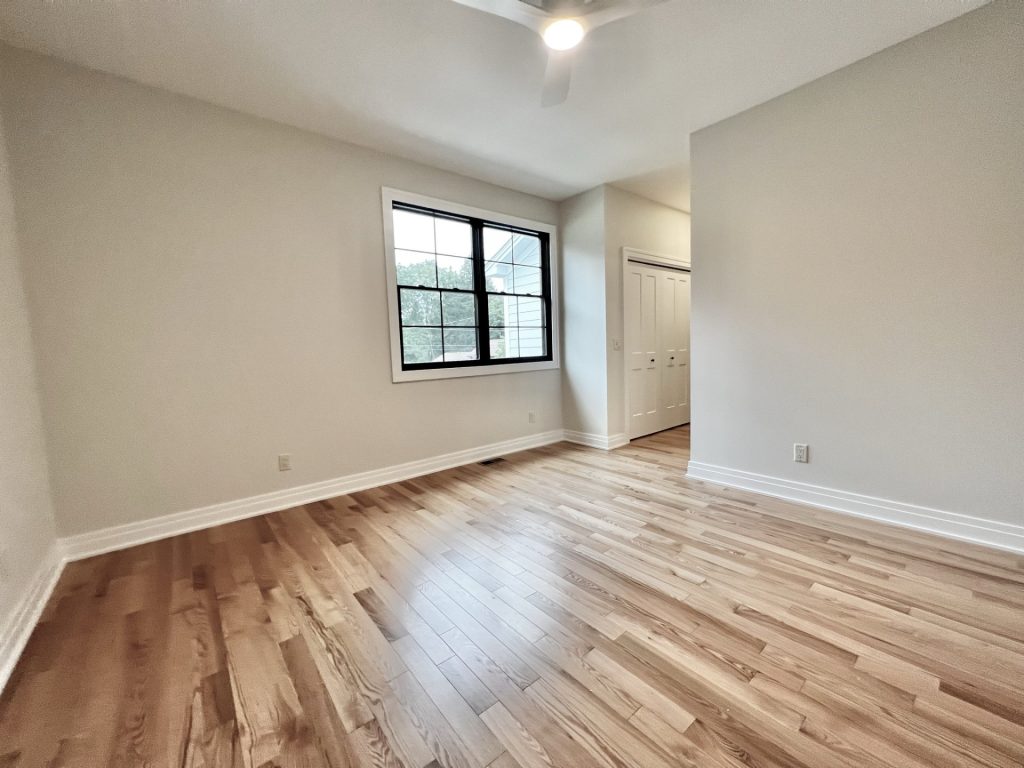 The Cedar Bedroom with Hardwood Flooring, Black-Framed Window, Double Closet Doors & Neutral Walls