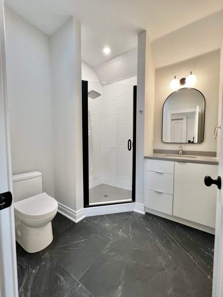 The Cedar Full Bathroom with White Vanity, Black-Framed Shower, Dark Tile Flooring & White Subway Tile Walls