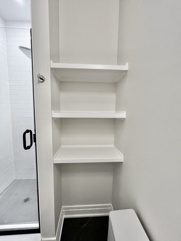 The Cedar Built-In Bathroom Shelving beside Black-Framed Shower with Dark Tile Flooring & Neutral Walls