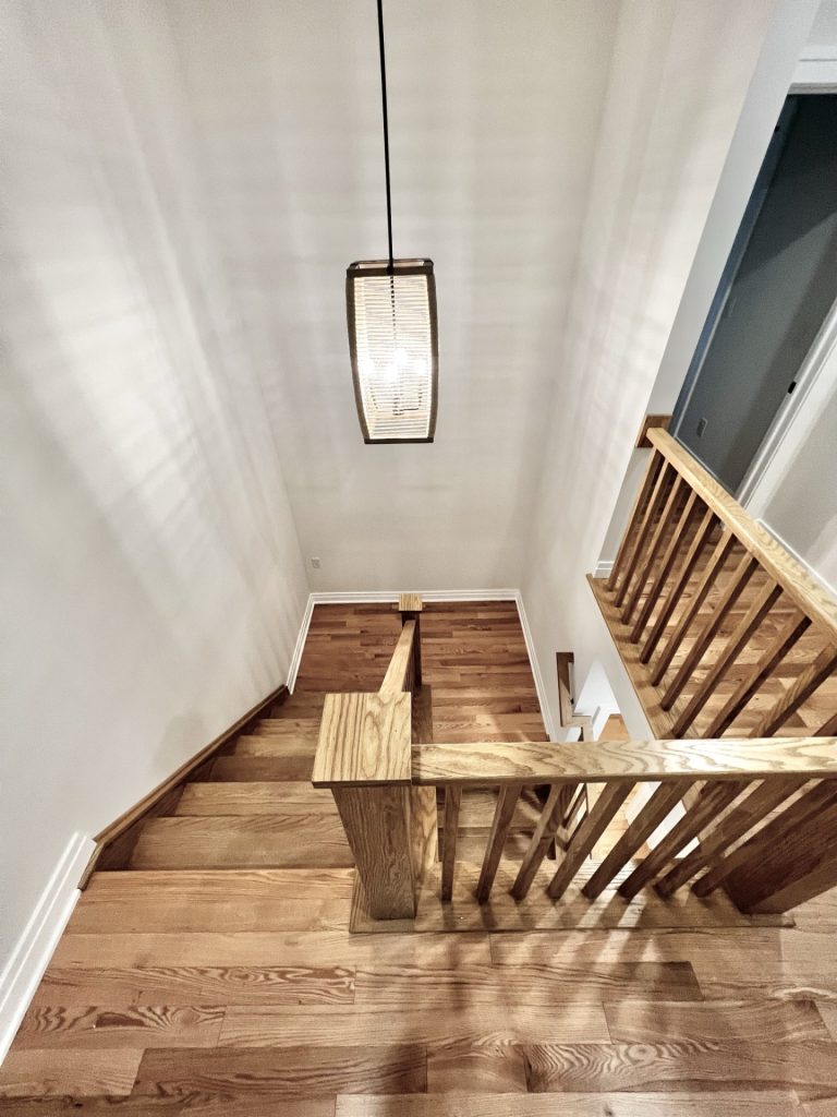 The Cedar Staircase View from Upper Landing with Wood Treads, Open Railing, Pendant Light & Neutral Walls
