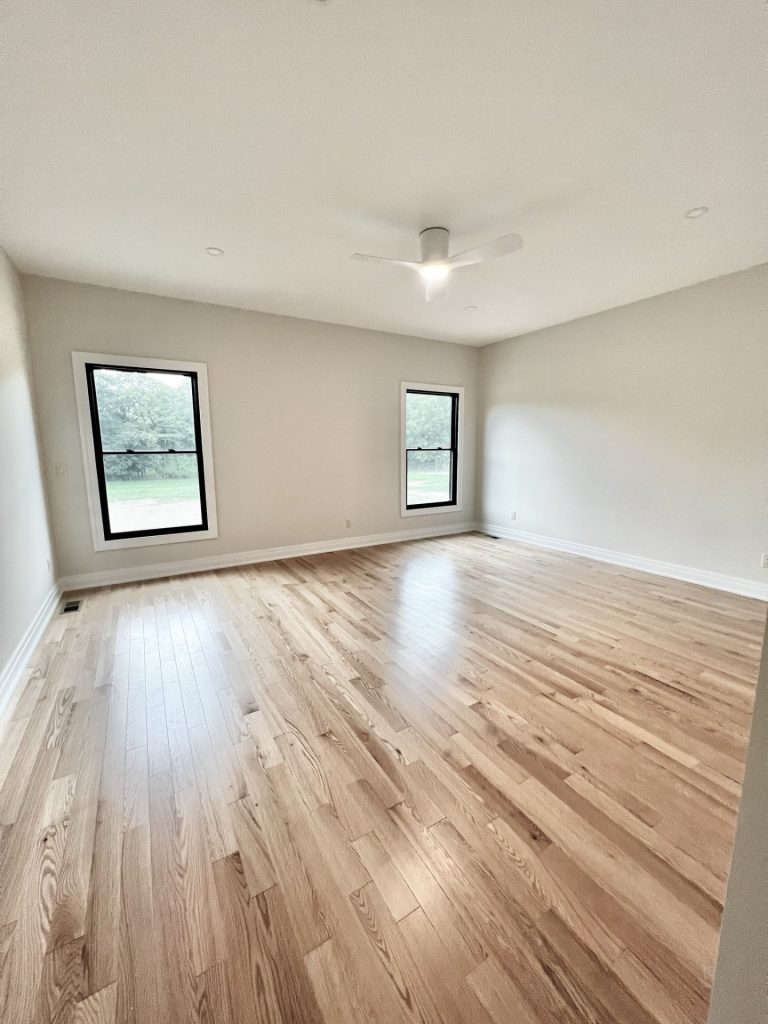 The Cedar Primary Bedroom with Hardwood Flooring, Ceiling Fan, Two Windows & Neutral Walls