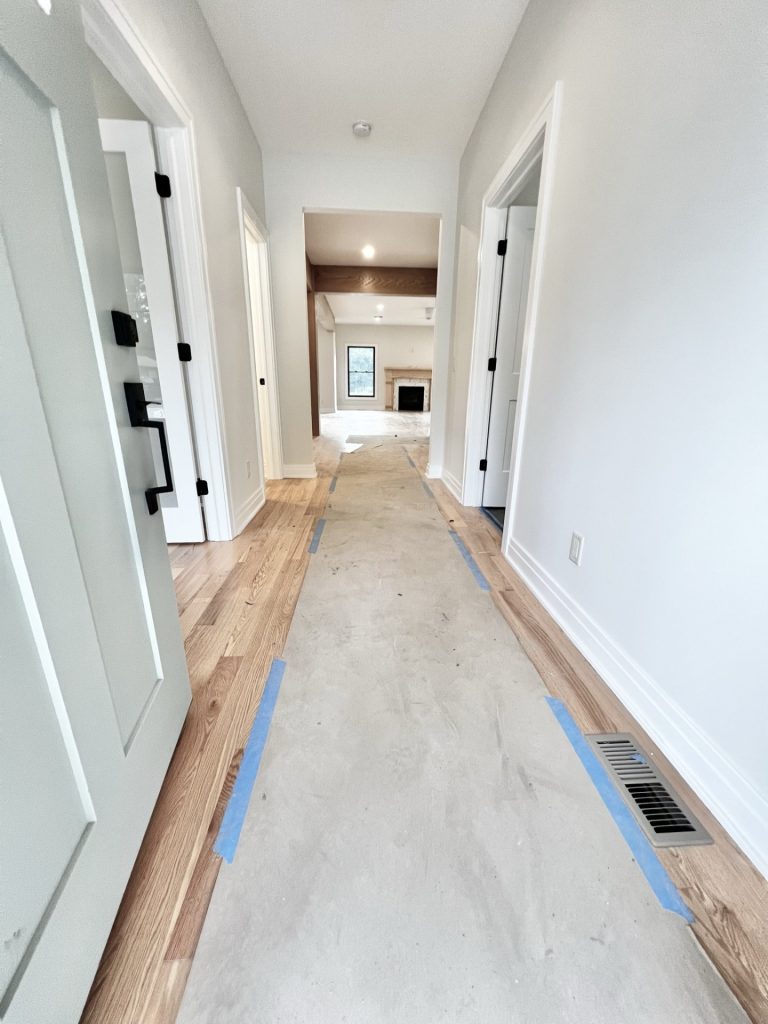 The Cedar Front Hallway with White Walls, Open Doors, Hardwood Flooring, and View of Fireplace in Great Room