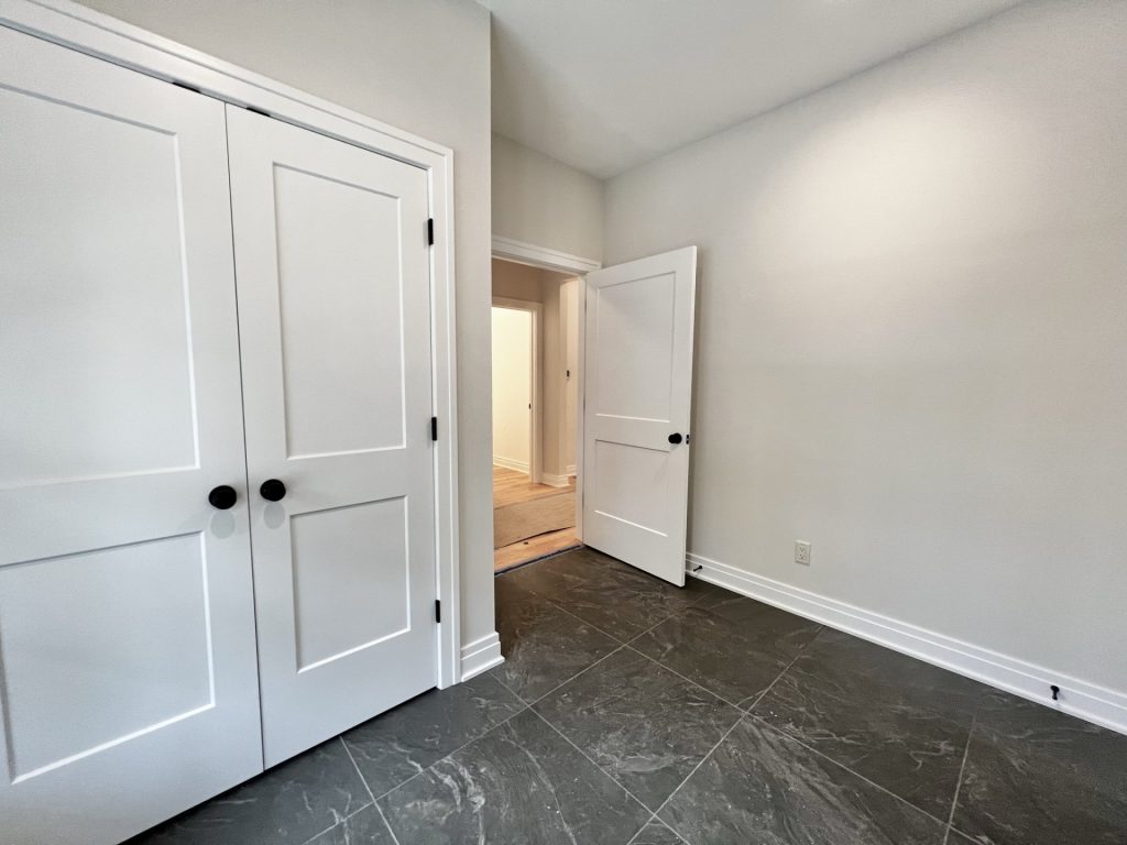 The Cedar Mud Room Corner with White Double Doors, Neutral Walls & Dark Tile Flooring