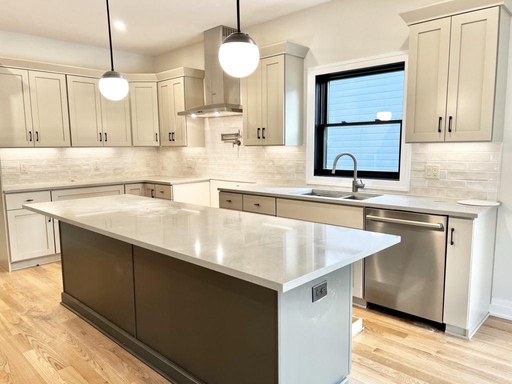 The Cedar Kitchen Sink Wall with Quartz Island, Light Cabinetry, Black-Framed Window & Tile Backsplash