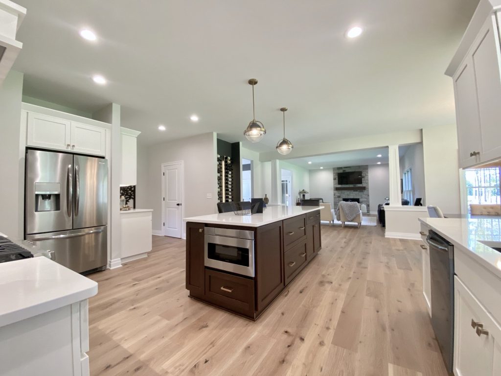 The Ruskin 2.0 Kitchen Island with Built-In Microwave, White Cabinetry, Wine Display Wall & Great Room Fireplace View