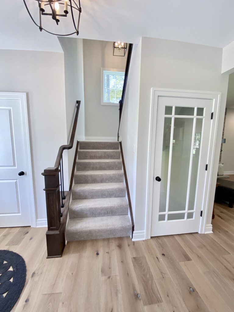 The Ruskin 2.0 Front Staircase with Carpeted Steps, Dark Handrail, Glass Door & Wood-Look Flooring