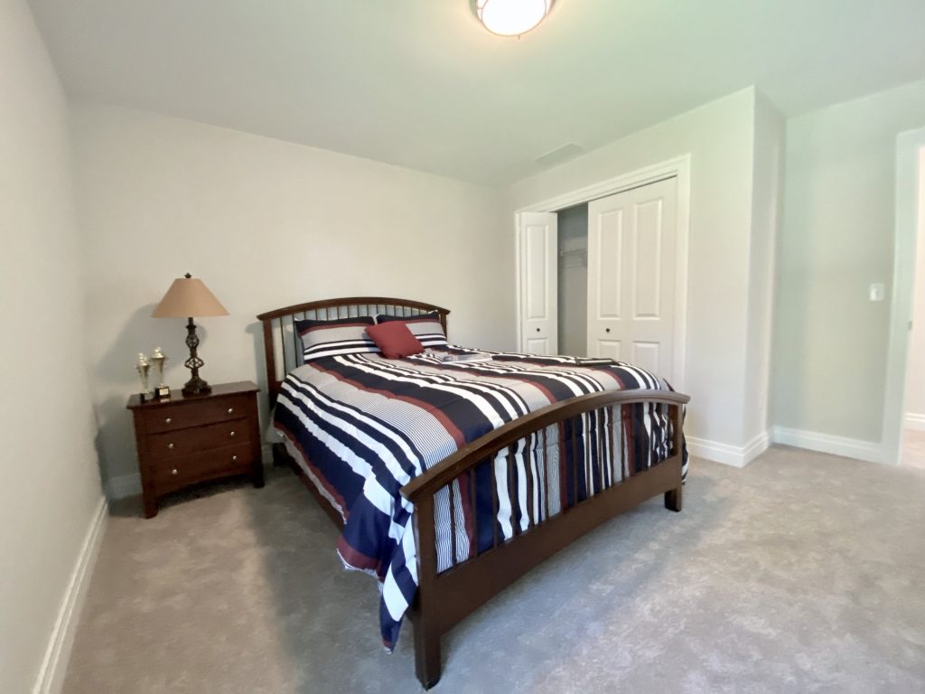 The Ruskin 2.0 Secondary Bedroom with Neutral Carpet, Dark Wood Bed, Open Closet & Nightstand