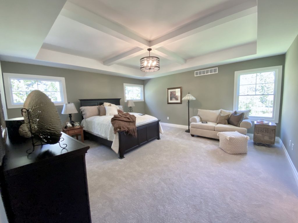 The Ruskin 2.0 Primary Bedroom with Coffered Ceiling, Sitting Area, Neutral Carpet & Two Windows
