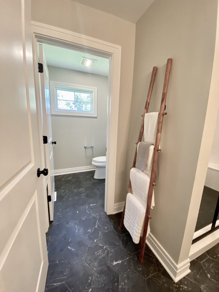 The Ruskin 2.0 Toilet Room Entry with Dark Hex Tile, Towel Ladder & Neutral Walls