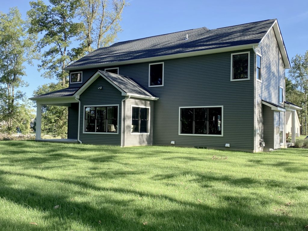 The Ruskin 2.0 Rear Exterior Angle with Covered Porch, Large Windows, Gray Siding & Backyard Lawn
