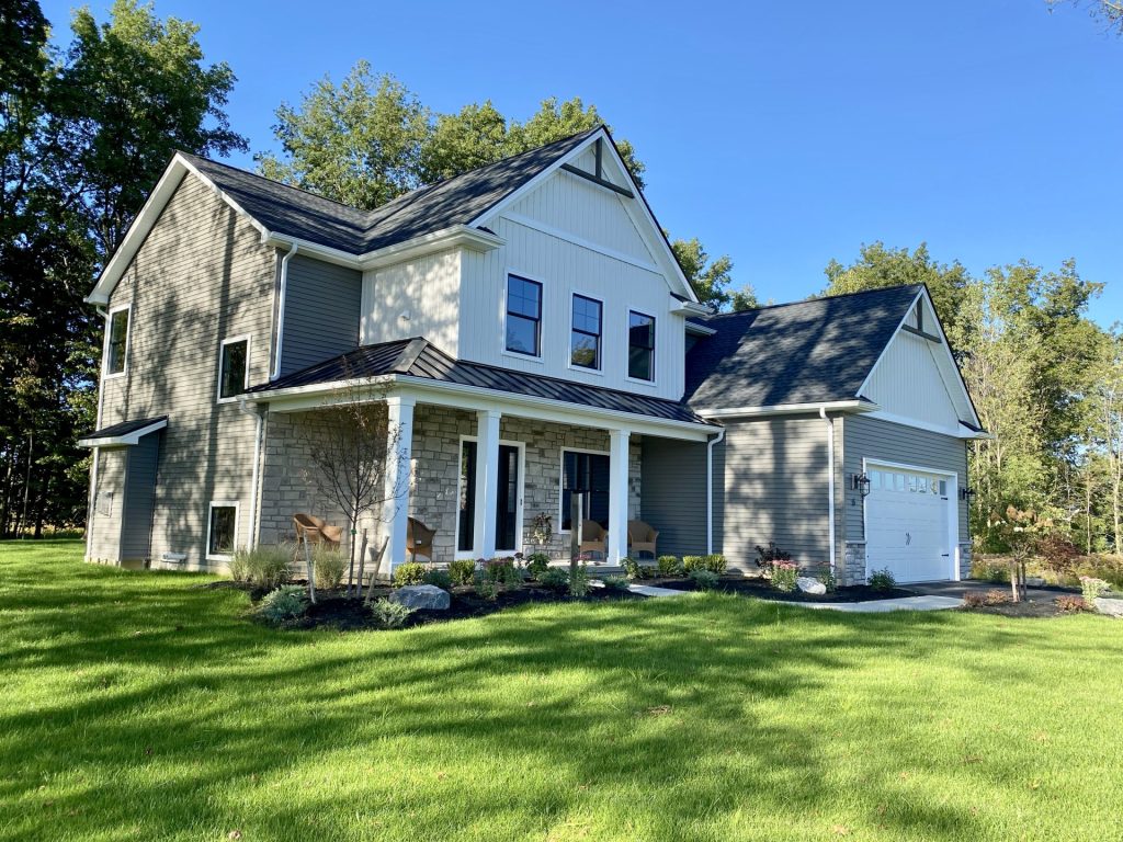 The Ruskin 2.0 Front Exterior Angle with White Gables, Stone Porch, Gray Siding & 2-Car Garage