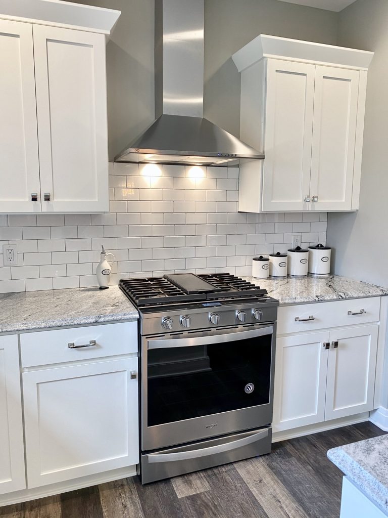 The Weston Kitchen Range Wall with White Cabinetry, Stainless Hood, Tile Backsplash & Quartz Counters