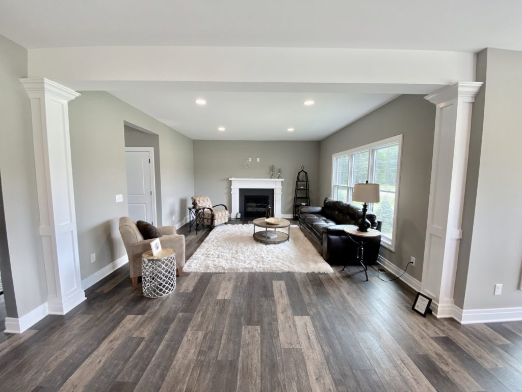 The Weston Great Room with Large Window, Fireplace, Gray Walls with White Trim & Wood-Look Flooring