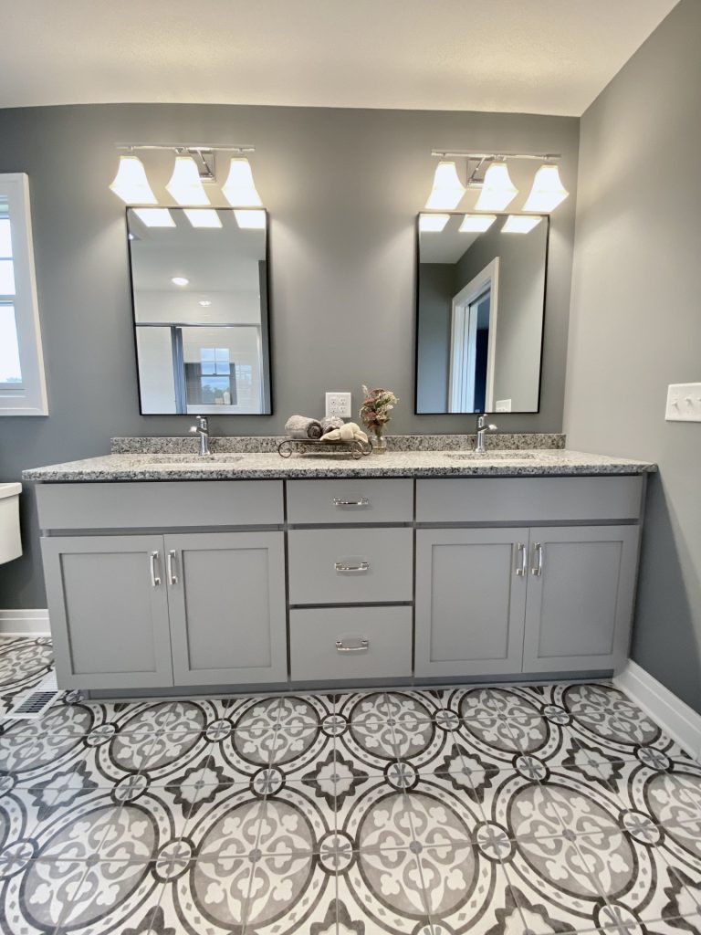 The Weston Master Bath Double Vanity with Gray Cabinetry, Granite Countertop, Patterned Tile Floor & Dual Mirrors