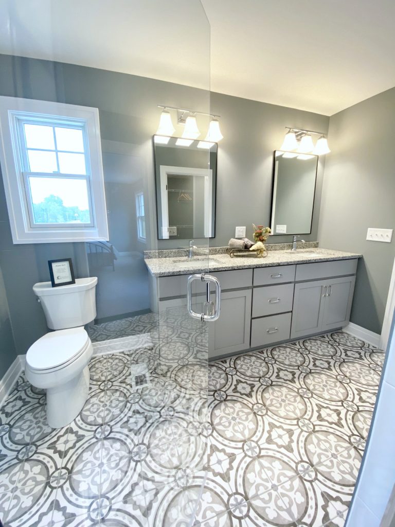The Weston Primary Bathroom with Toilet, Double Vanity, Patterned Tile Floor, Glass Shower Door & Gray Walls