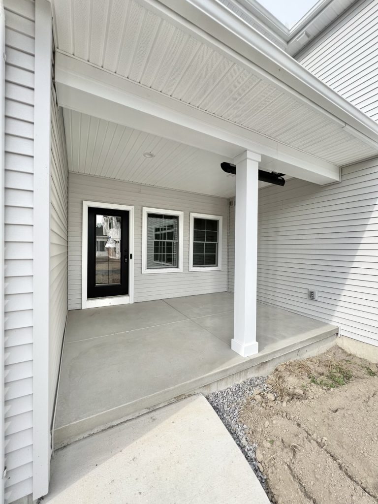 The Willow Covered Rear Porch with Black Door, White Columns, Concrete Patio & Light Gray Siding